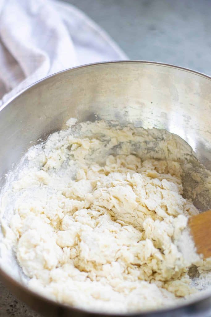 Bun dough being mixed in a stainless steel bowl with a wooden spoon.