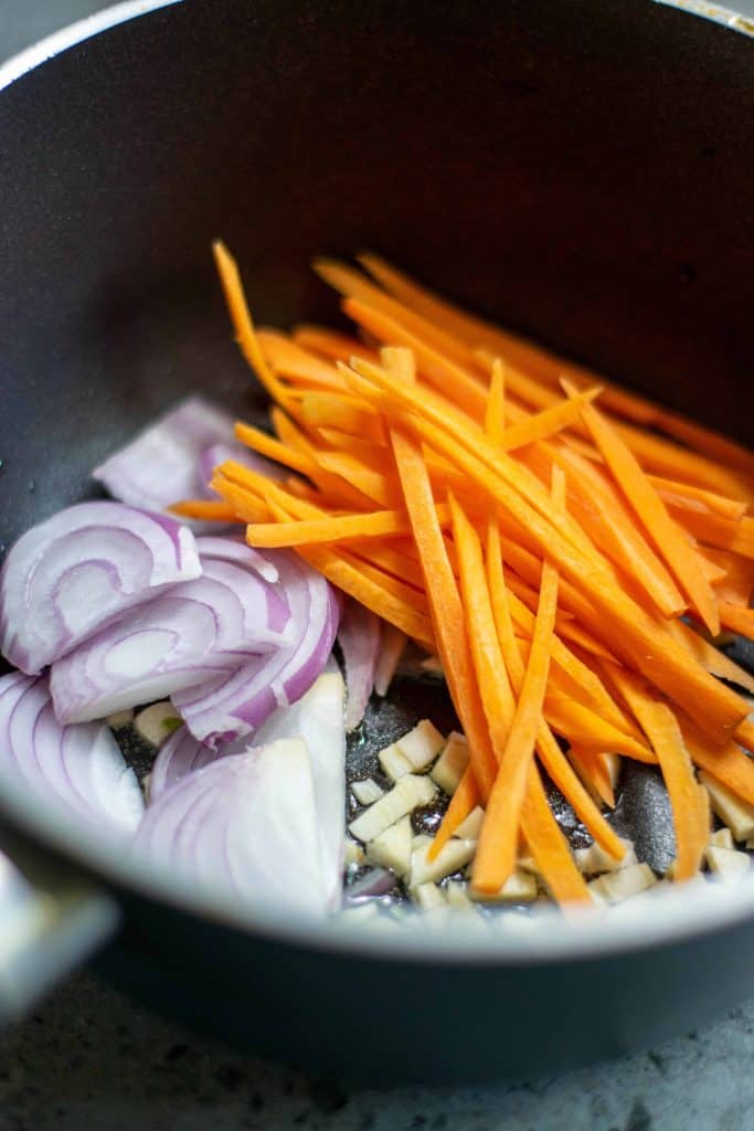 Carrots, red onion and garlic in a frying pan.