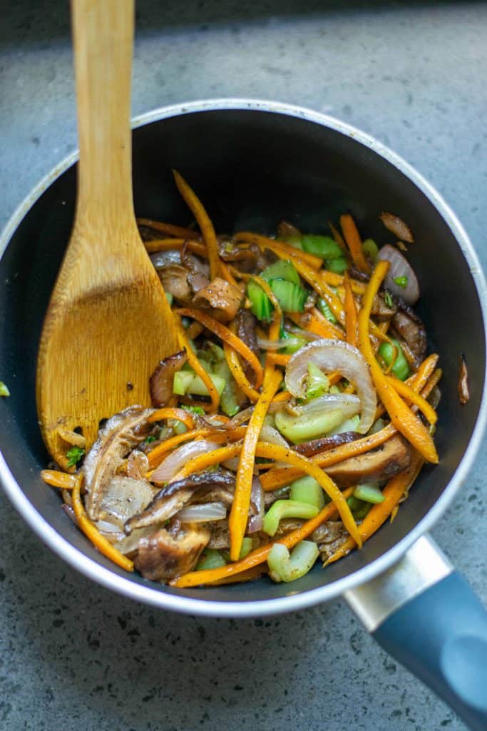 Carrots, onion, garlic, Bok Choy stems and shiitake mushrooms in a frying pan.