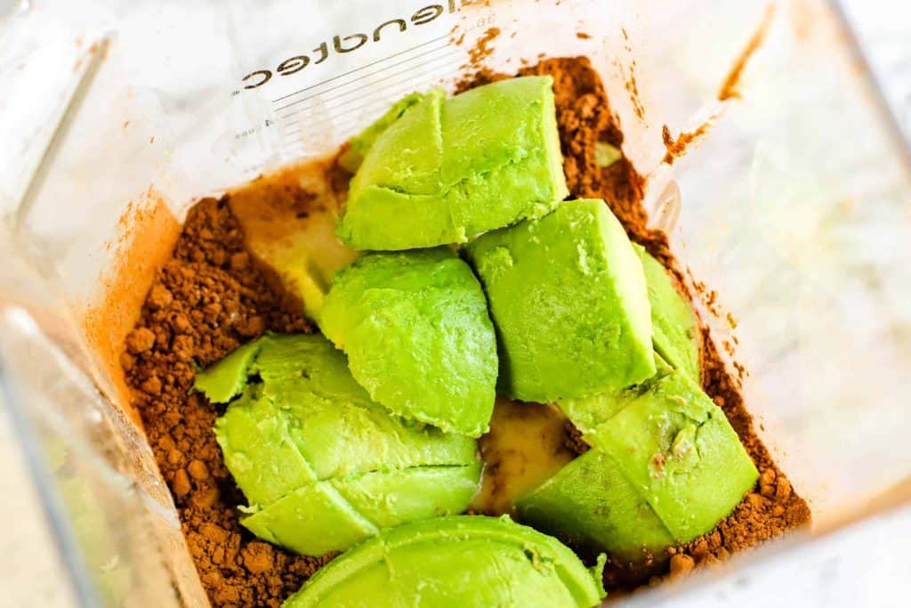 Avocado in blender on top of cocoa and coconut milk.