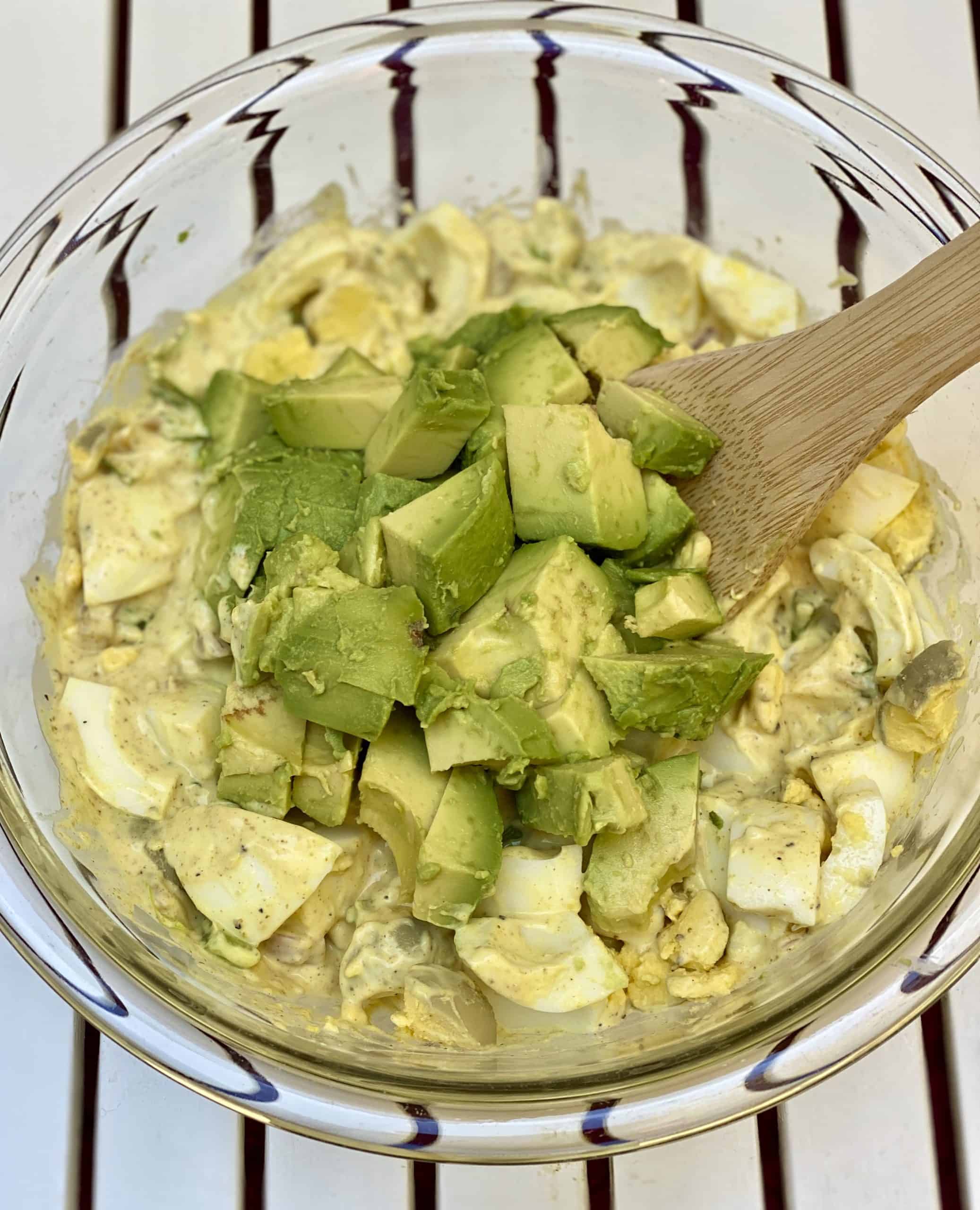 avocado egg salad being stirred in a glass bowl.
