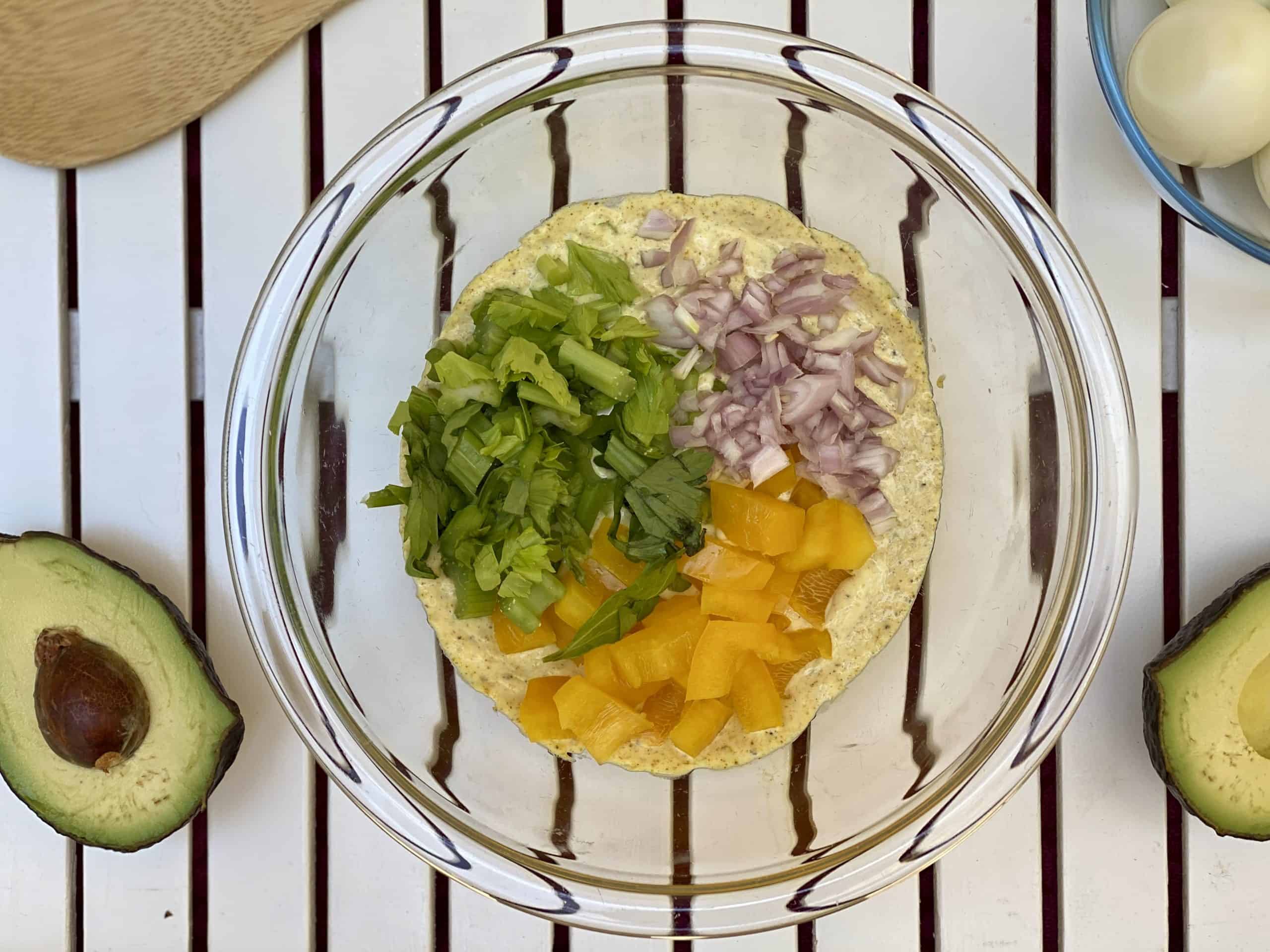celery, bell pepper and shallots on top of mayo dressing in a glass bowl.