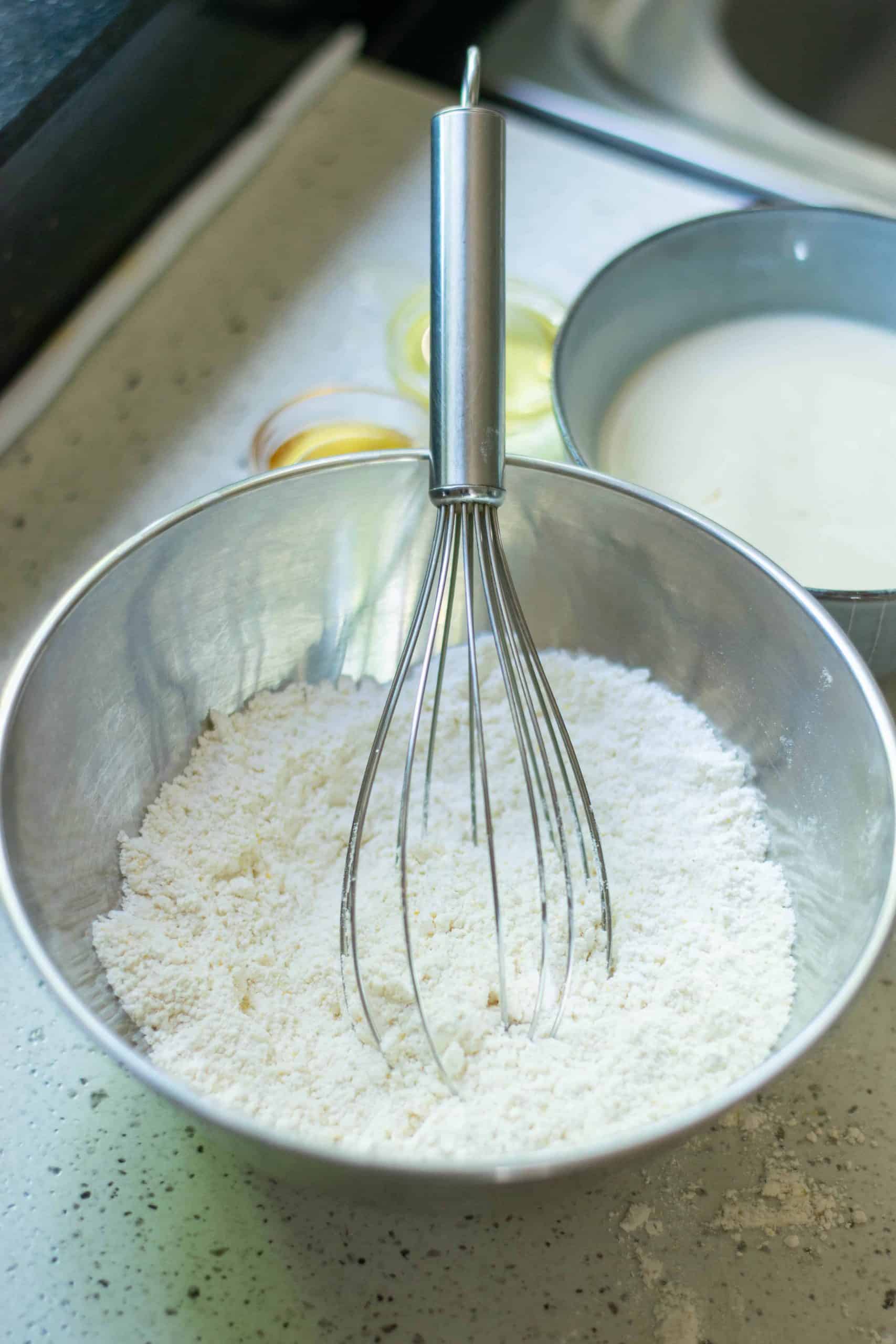 Flour in a stainless steel bowl with a whisk in it.