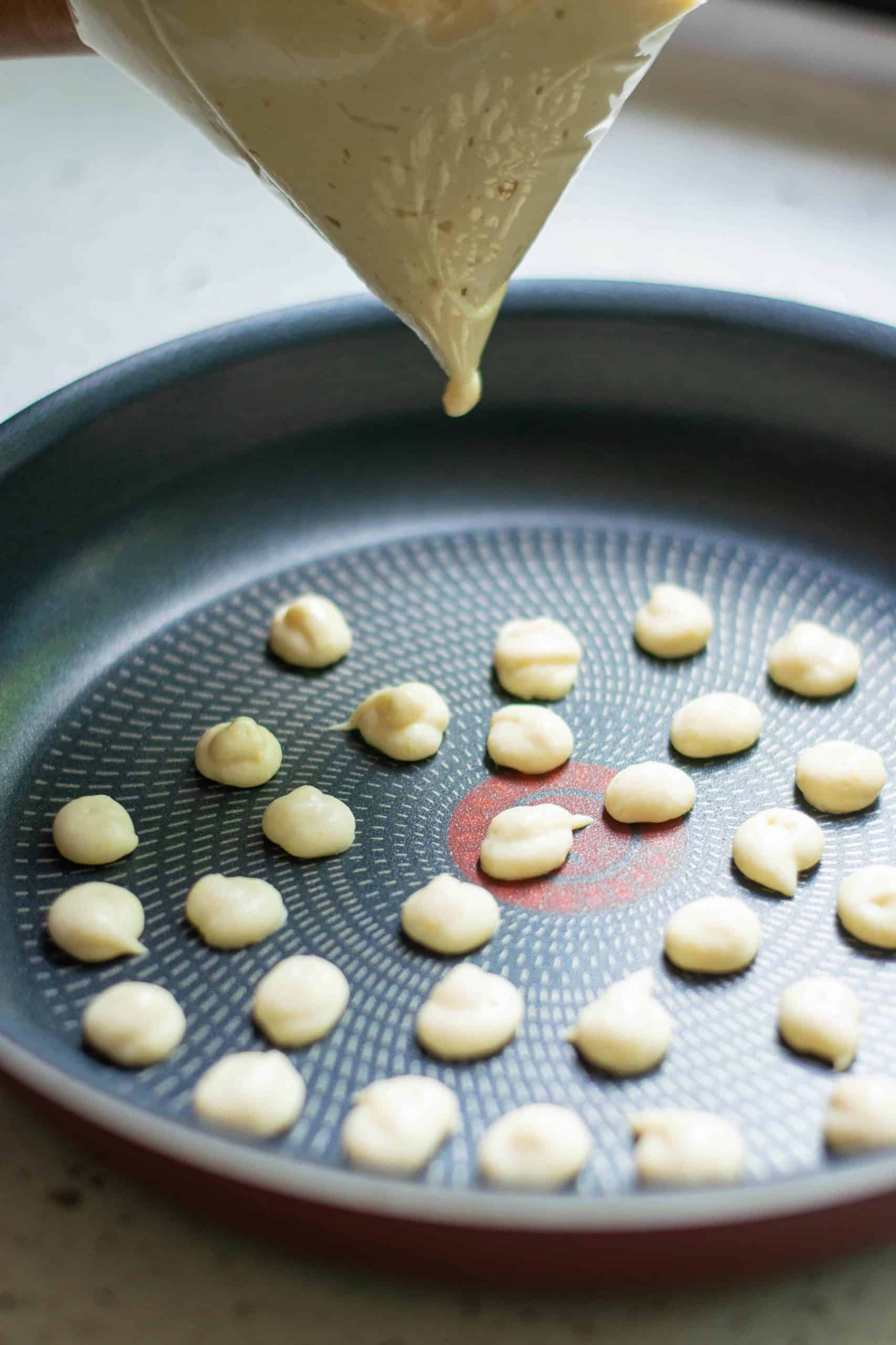 Pancake batter poured into a pan in mini circles.