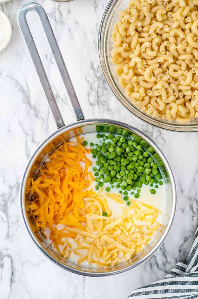 Peas, cheddar cheese and gouda cheese in a saucepan with macaroni in upper righthand corner.