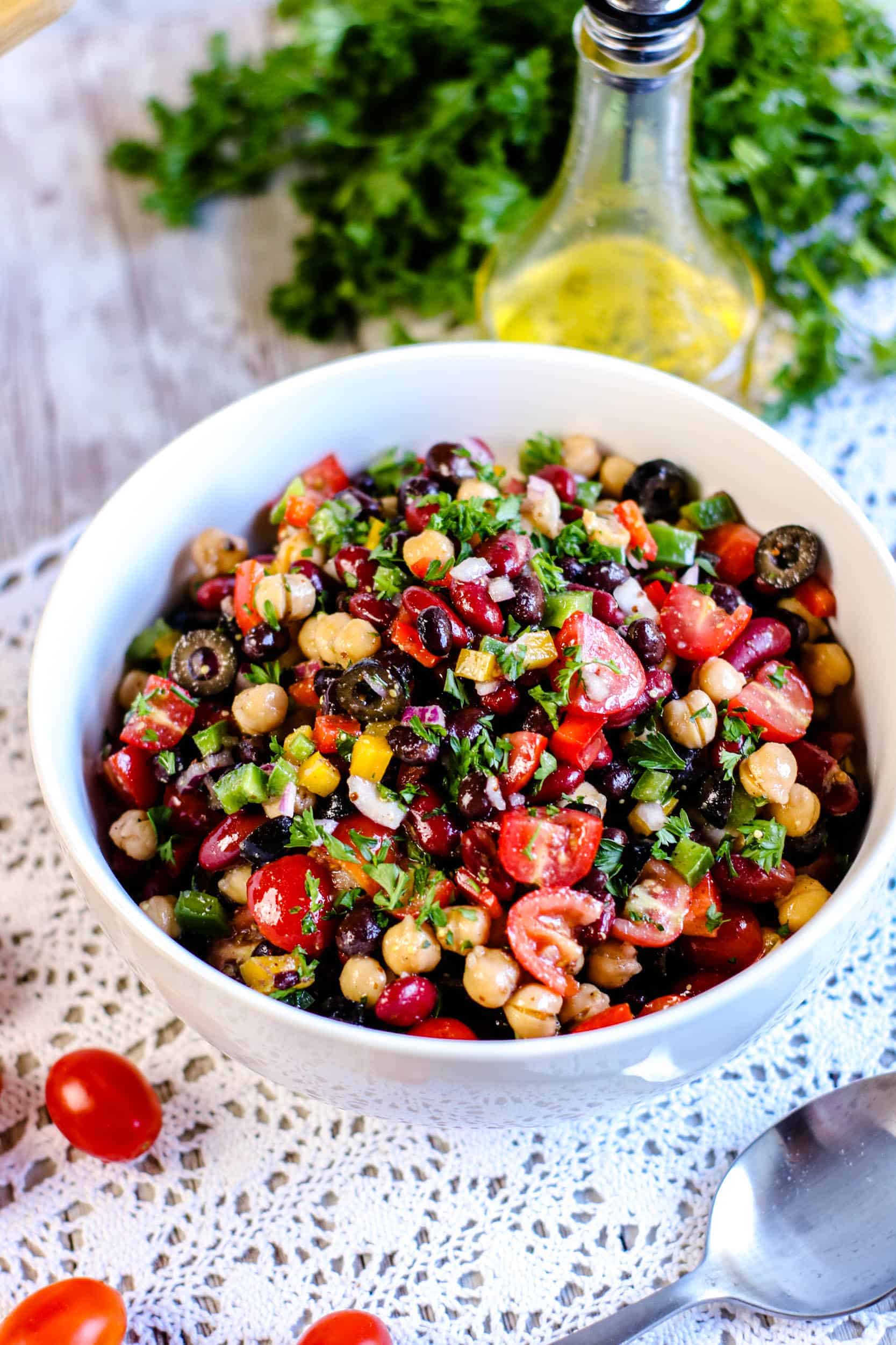 Rainbow Three Bean Salad in a large white bowl with bottle of dressing behind it.