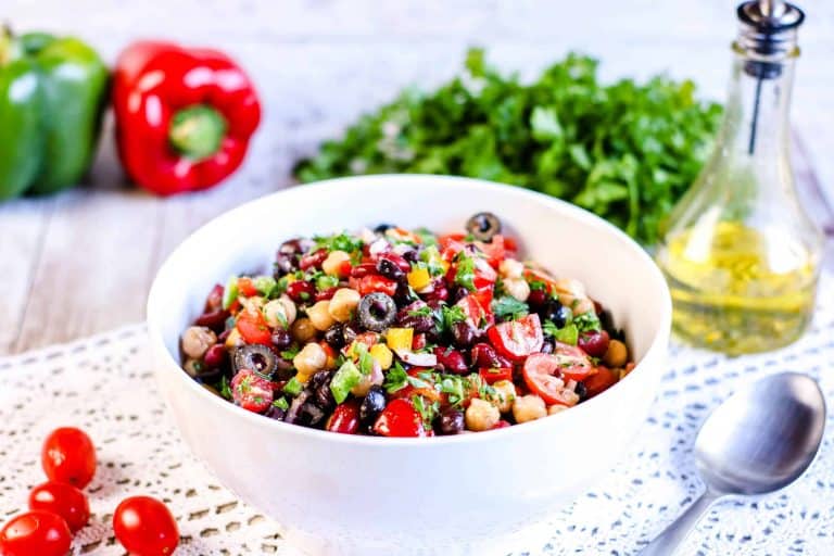 Rainbow Three Bean Salad in a white bowl iwht spoon on the right and dressing in the back corner.