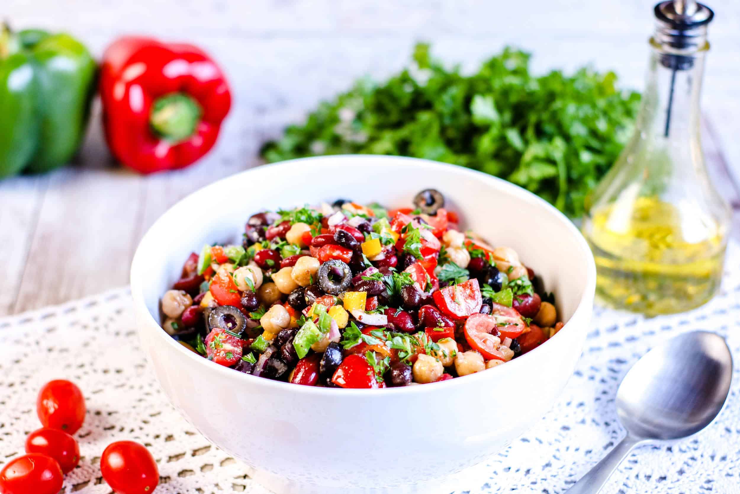 Rainbow Three Bean Salad in a white bowl iwht spoon on the right and dressing in the back corner.