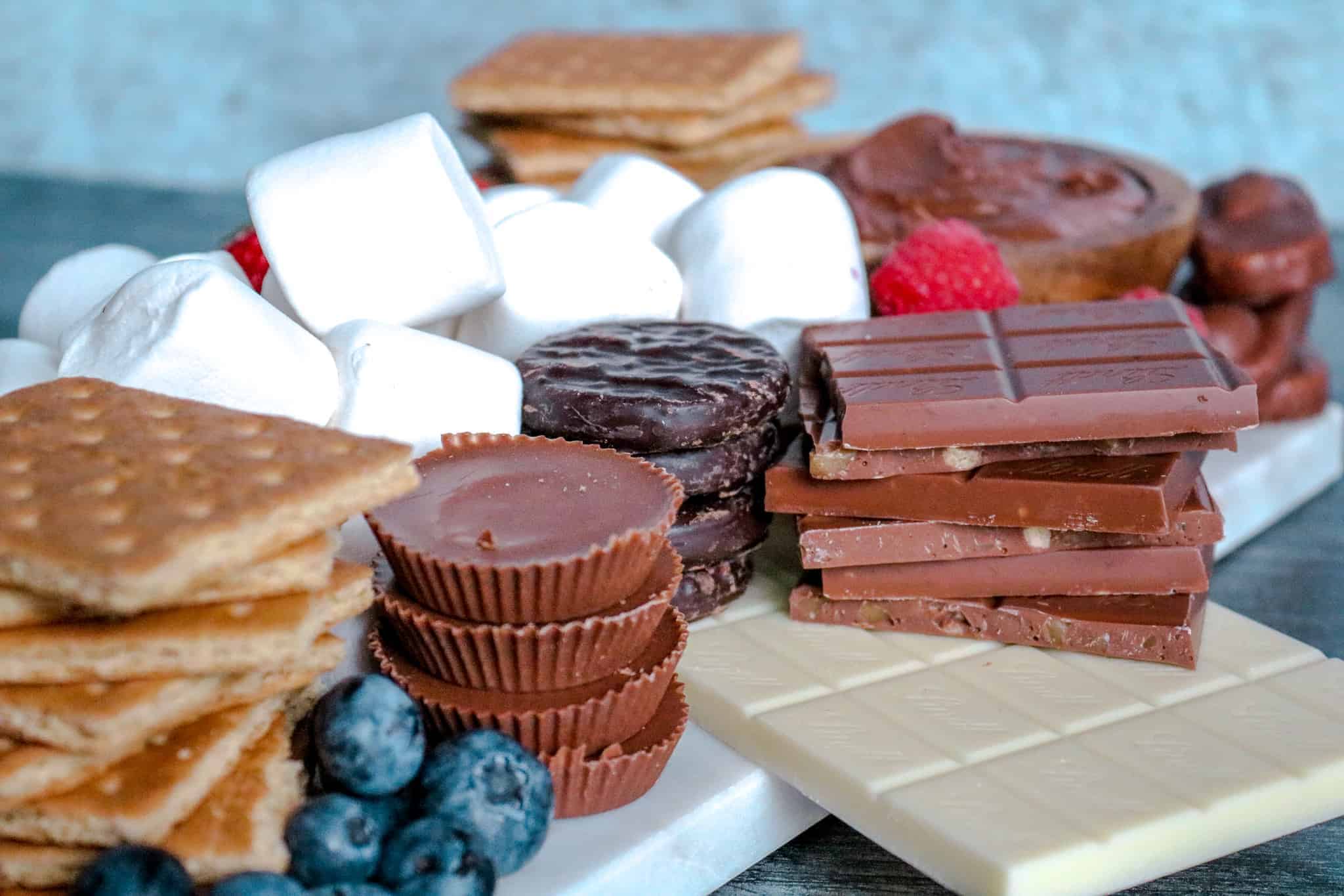 ¾ angle shot of chocolate candy, marshmallow and fruit on a white marble board.