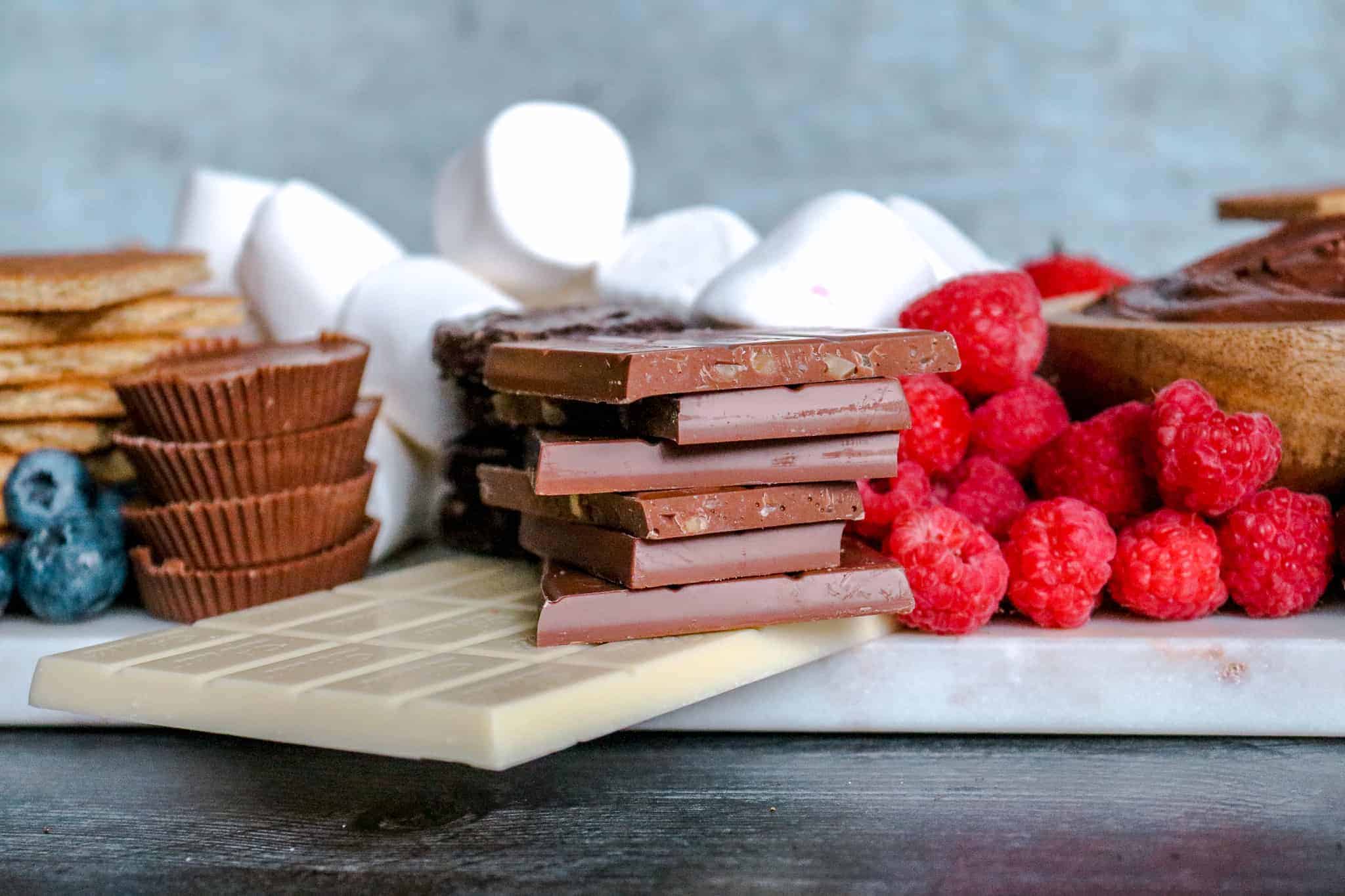 How to Make a Loaded S'mores Board: head on shot of chocolate bars, peanut butter cups, raspberries, blueberries and marshamllows