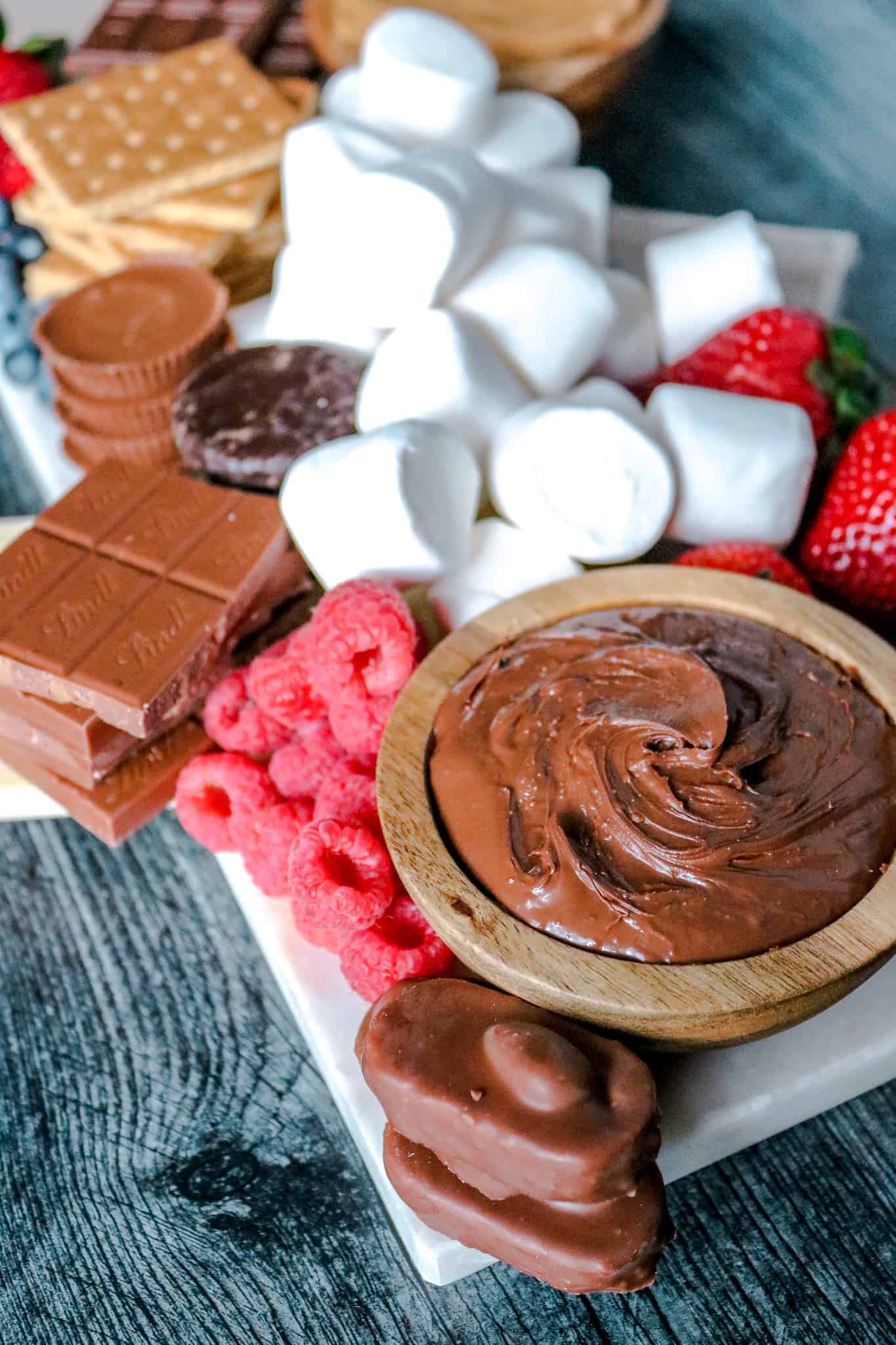 Closeup of Nutella, almond joy bars, marshmallow and fruit on white marble slab.