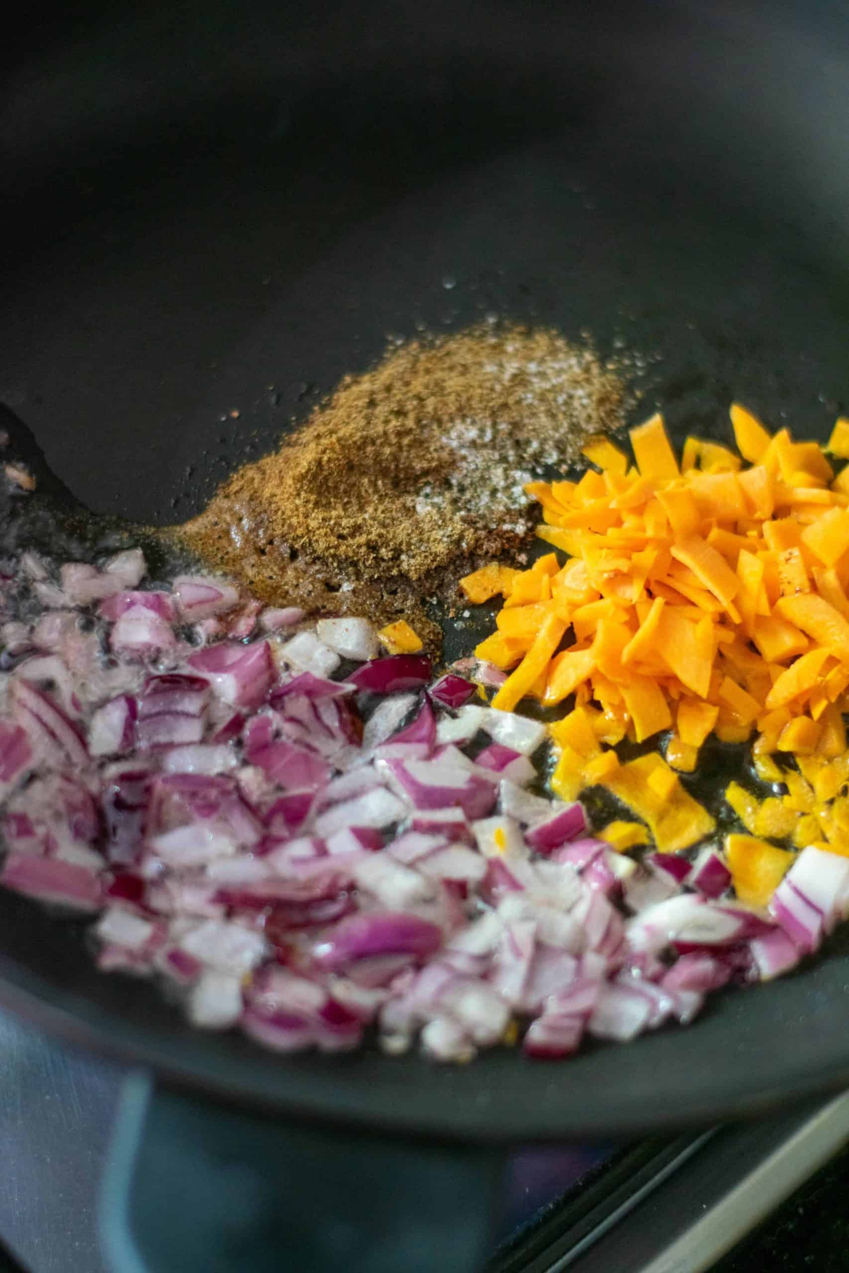 red onion, carrots and spices in a frying pan.