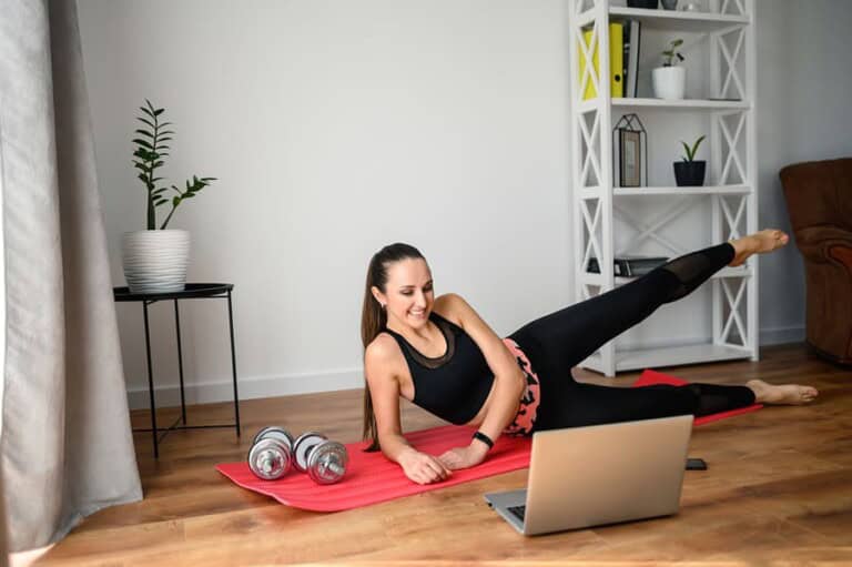Doing sports at home during quarantine. Stay home. Workout video tutorial. A young girl does exercises and looks at the screen of a laptop. Concept of online learning, full at home workout video
