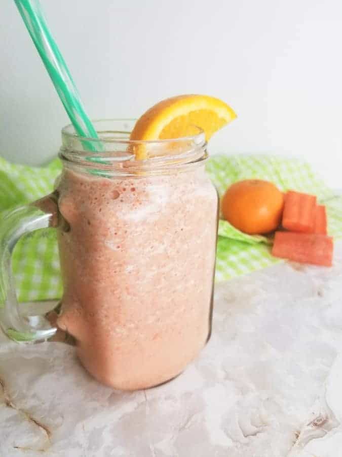 Carrot Orange Smoothie in a glass mug with an orange slice and a green striped straw.