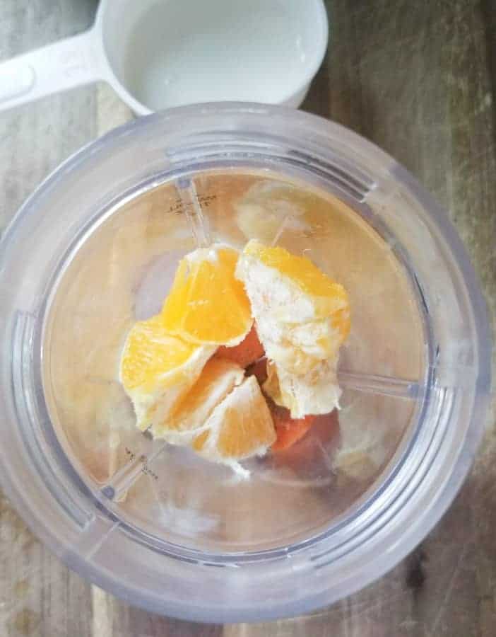 Overhead shot of blender with oranges, carrots, ice and flax seed and a white measuring cup off to the side.