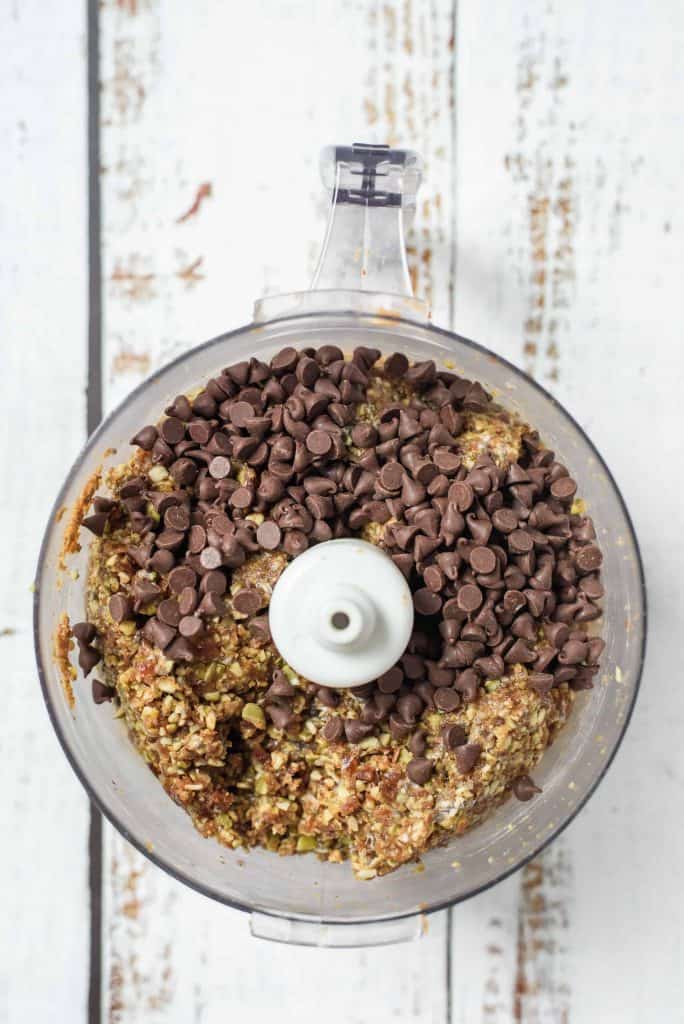Chocolate chips on top of processed nuts in a food processor.