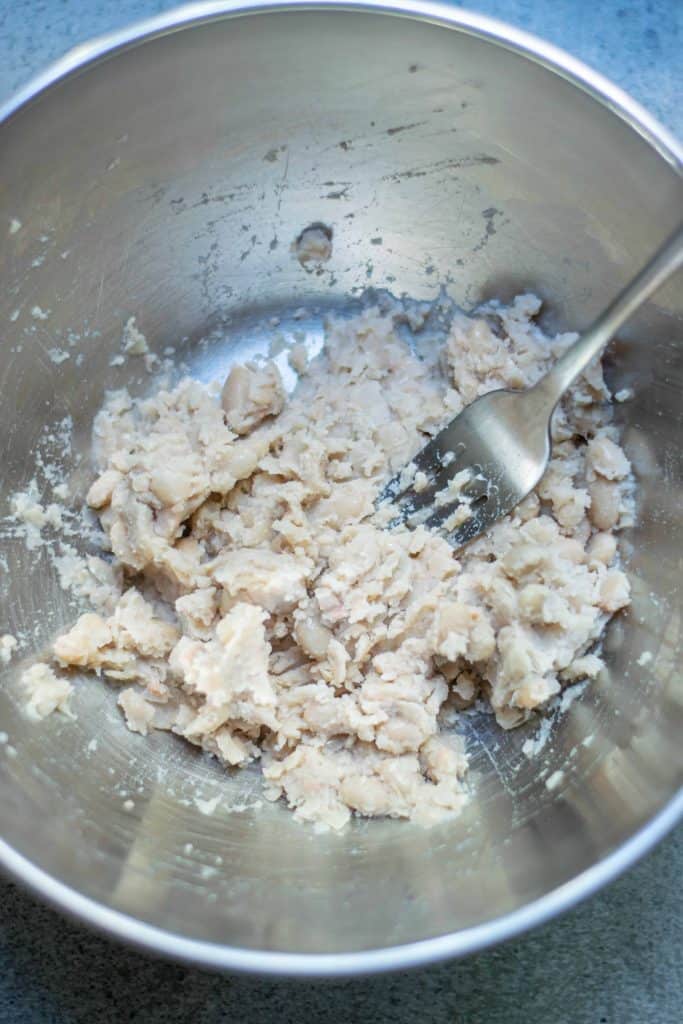 Mashed white beans in a stainless steal bowl.