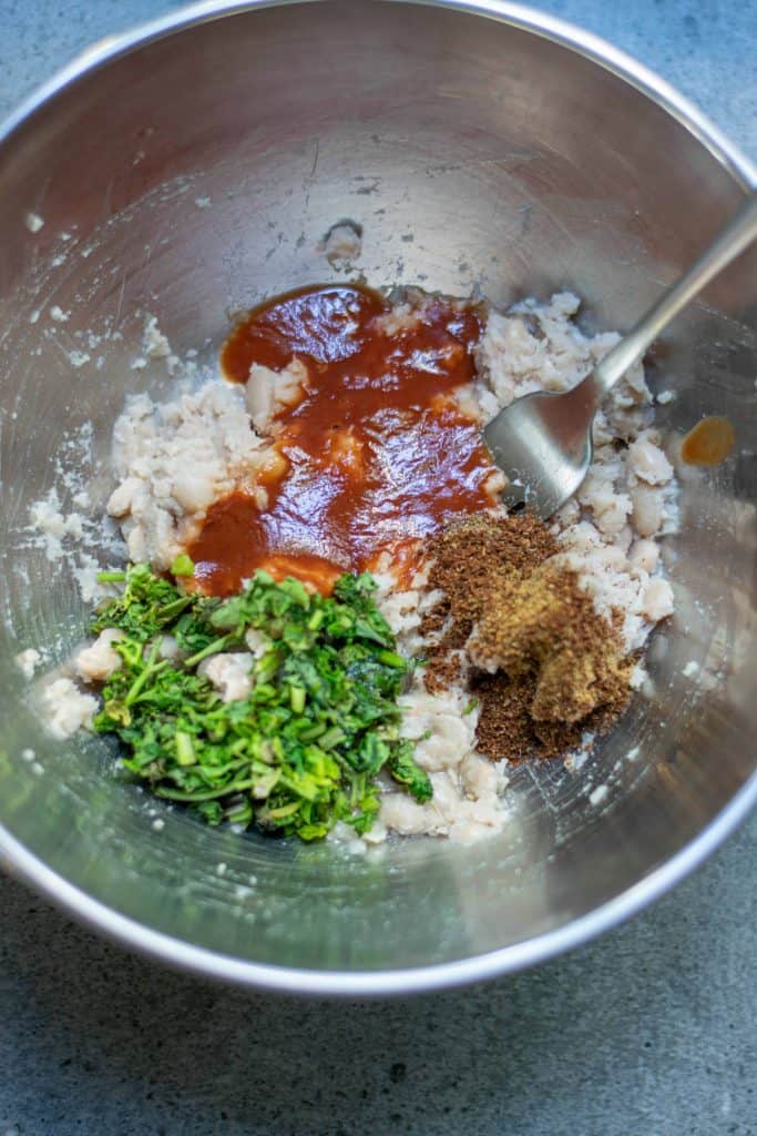 mashed white beans, spices, cilantro, onions and pureed tomatoes in a stainless steel bowl.
