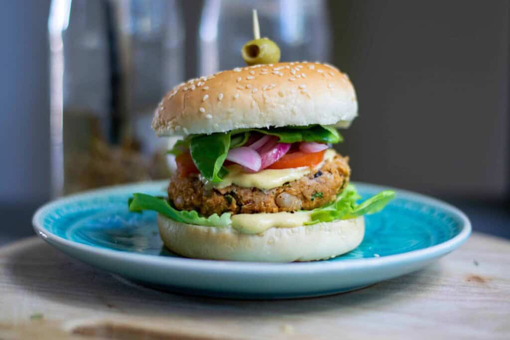 Vegan white bean burger on a Lue plate with an olive on top.
