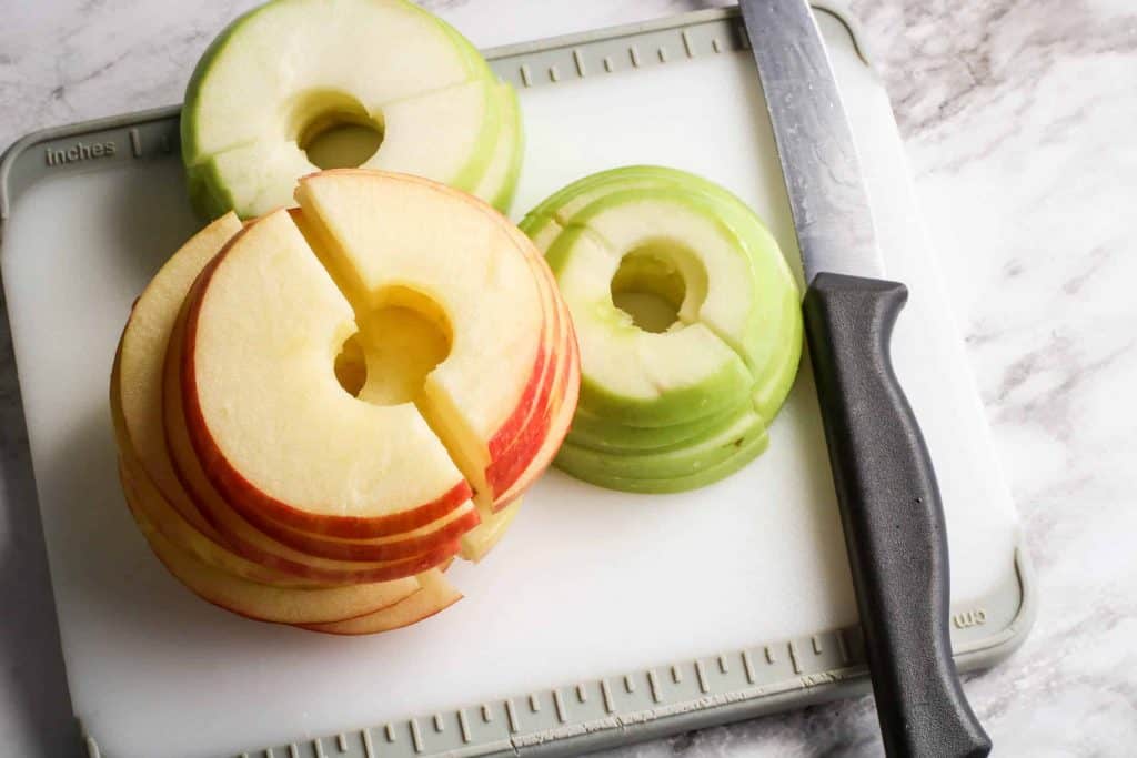 Sliced Macintosh and Granny Smith Apples on a cutting board with a knife on the right side.
