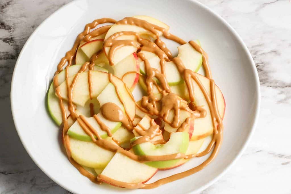 Apple slices on a white plate drizzled with peanut butter.