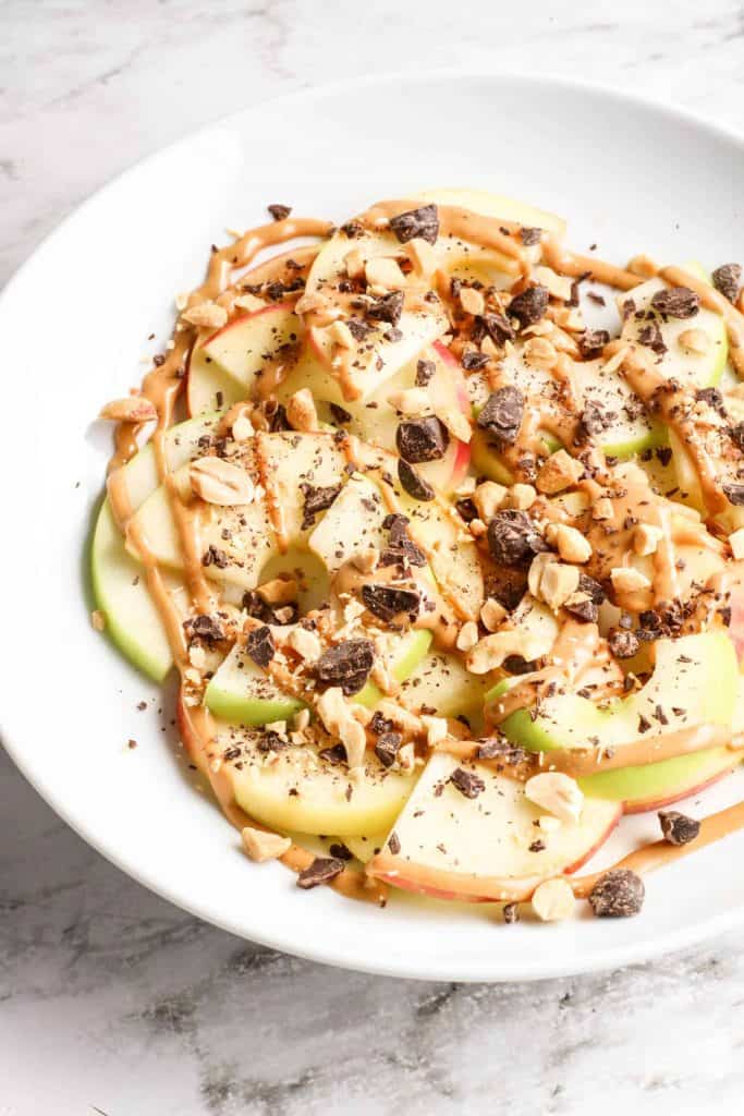 Apple nachos on a white plate with marble background.