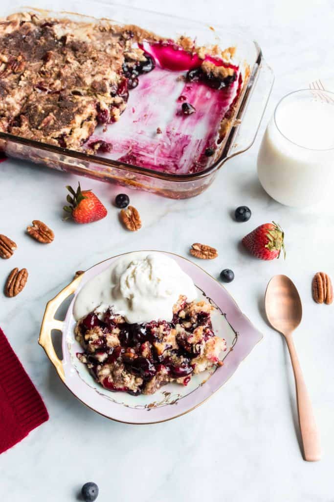 Baked Blueberry Strawberry Dump Cake in baking dish with a serving of it on a plate a la mode.