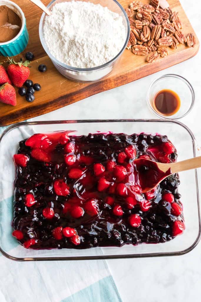 Overhead photo of blueberry and cherry pie filling in a 9x13 glass baking dish with a spoon in it.