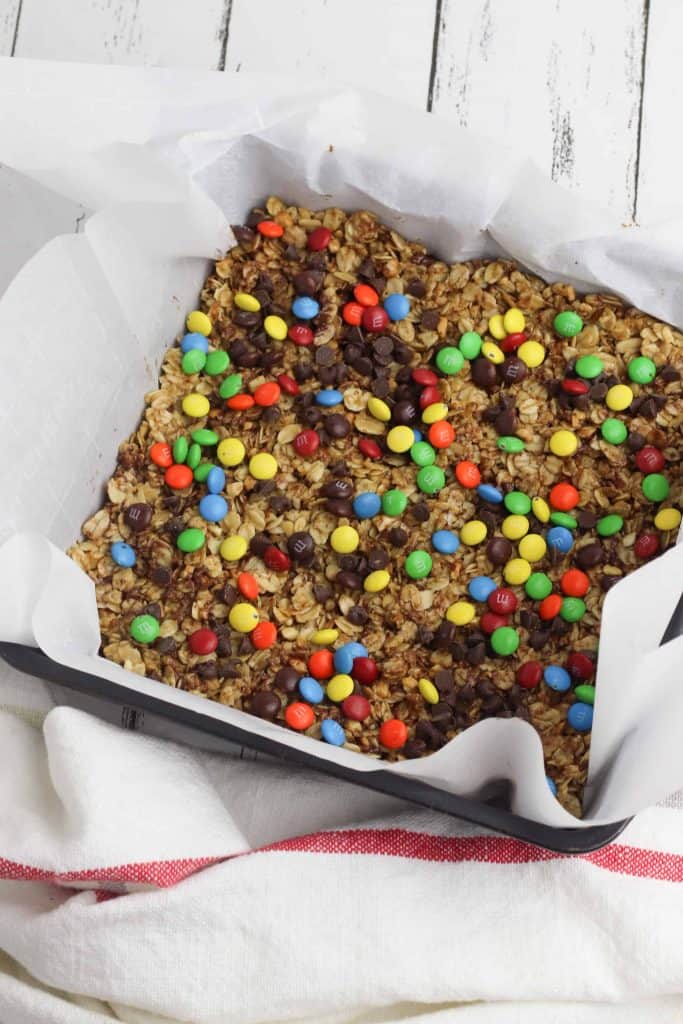 Granola topped with chocolate chips in a baking pan lined with parchment paper.