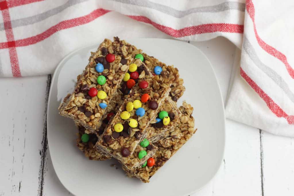 Chocolate Chip Granola Bars on a whit plate on white wood with a white kitchen towel above them with red and gray stripes.