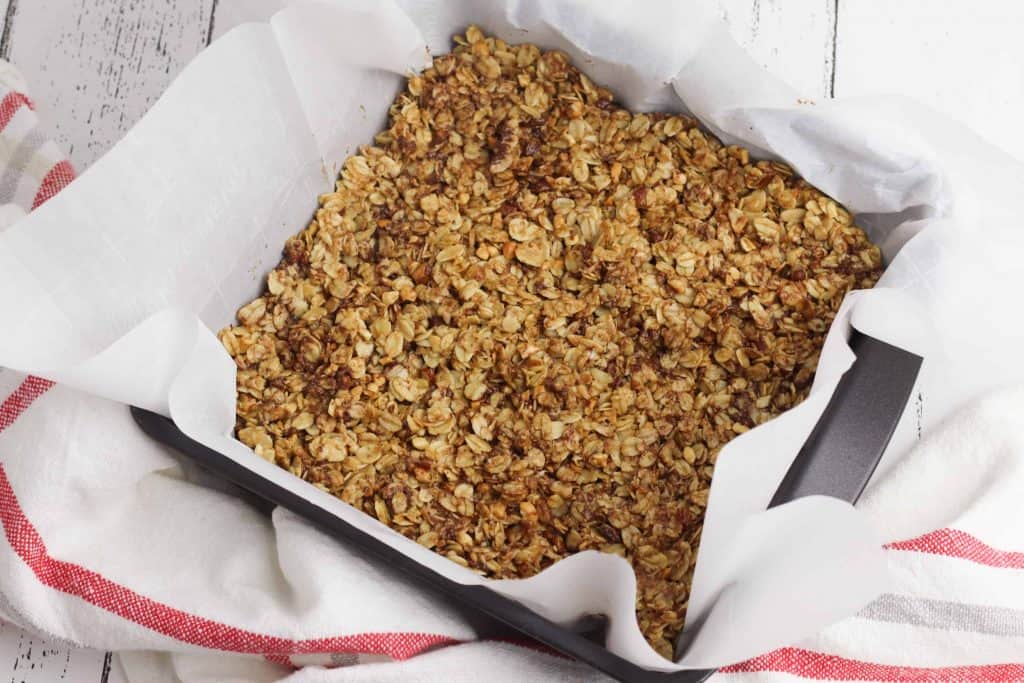 Granola pressed into a baking pan lined with parchment paper on white wood.