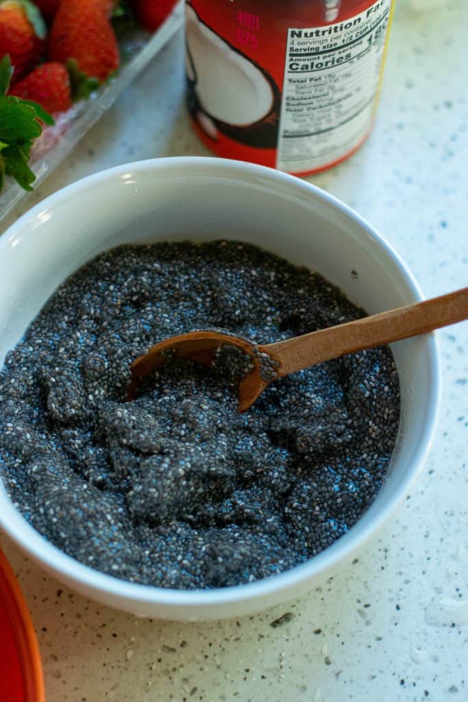Chia seeds being soaked in a bowl of water with a wooden spoon in the bowl.