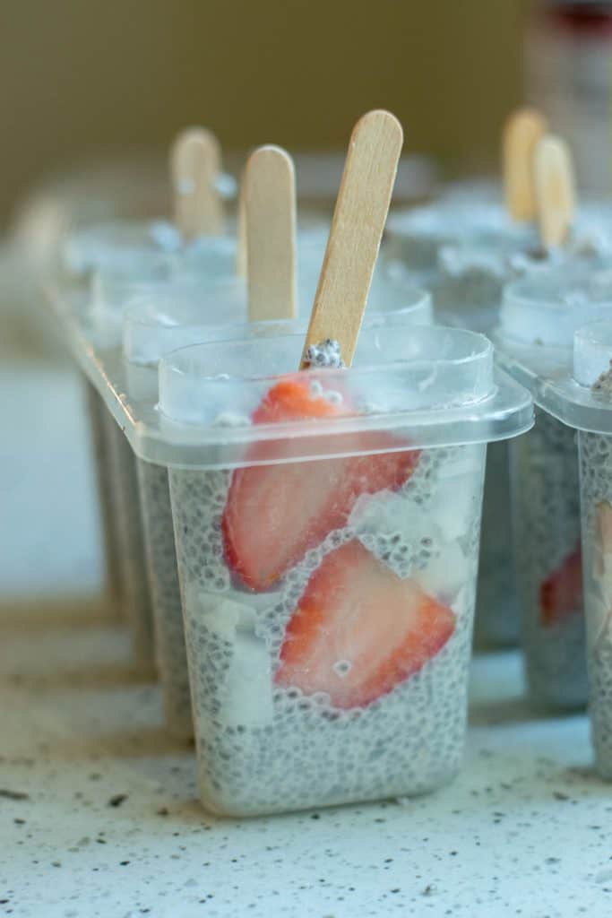Chia seed pudding popsicle with strawberries in popsicle mold with popsicle sticks in them.