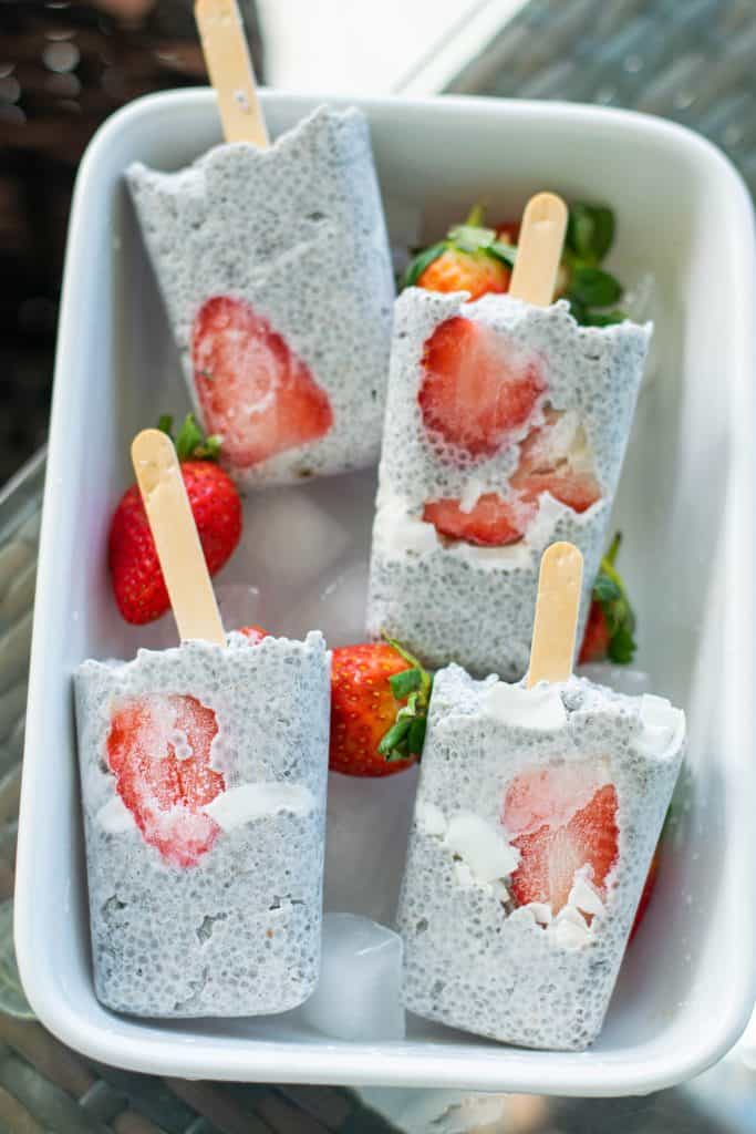Creamy Coconut Chia Seed Popsicle with Strawberries in a white ceramic dish with ice and fresh strawberries.
