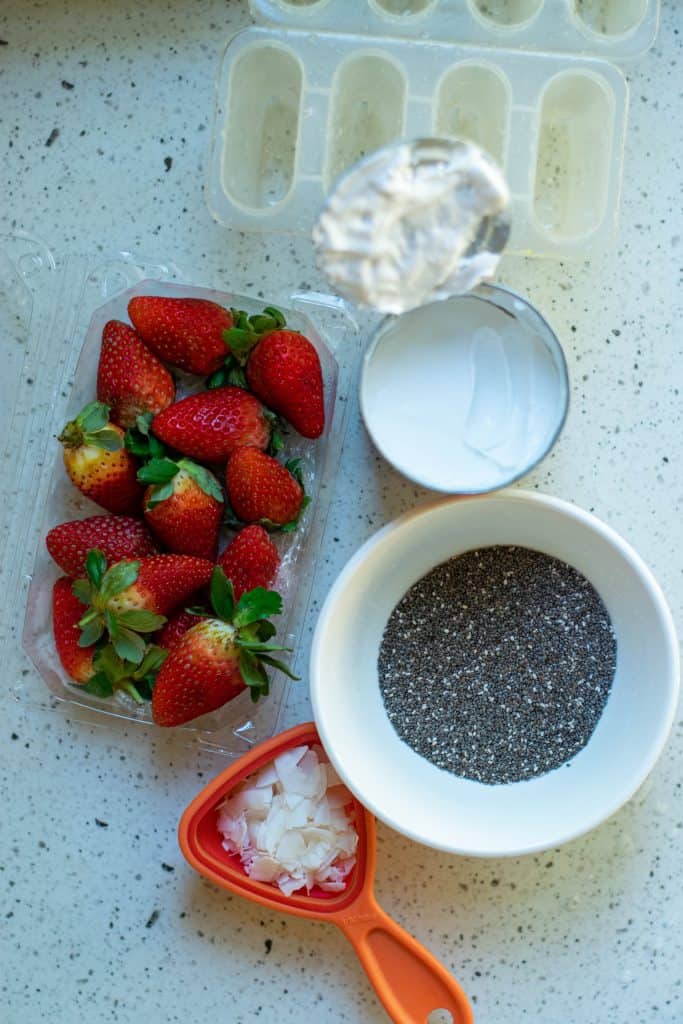 Overhead shot of strawberries, chia seeds, coconut cream, shredded coconut and popsicle mold