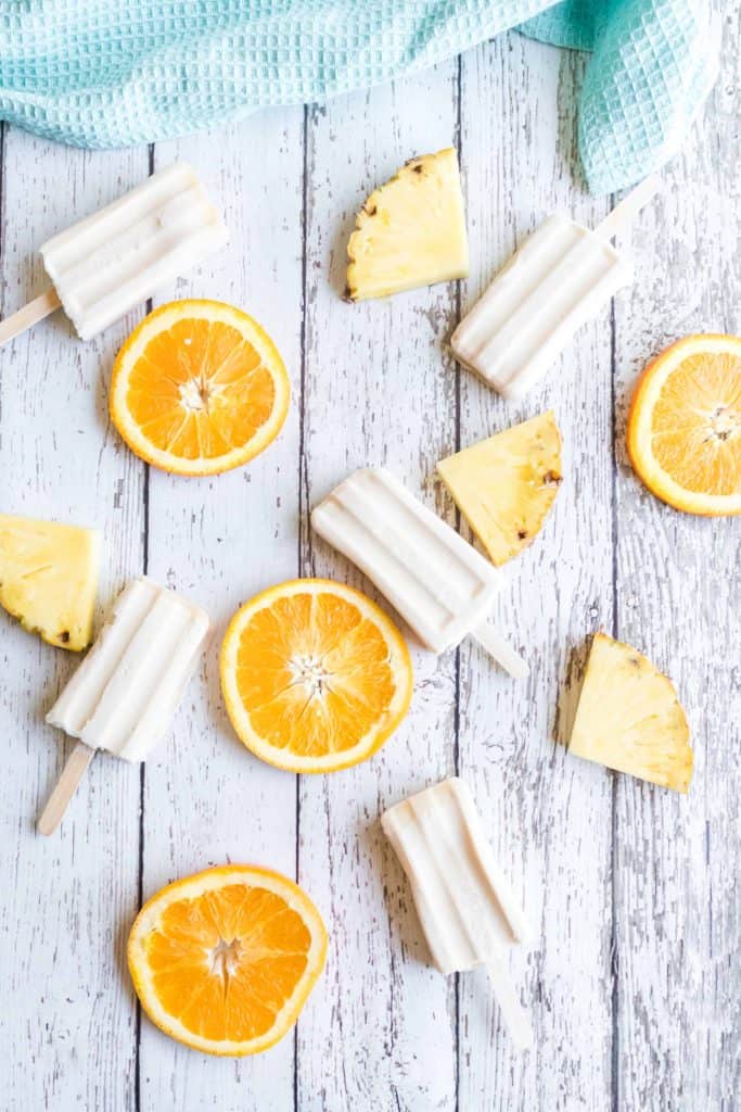 Popsicles on a white board with orange slices and pineapple chunks.