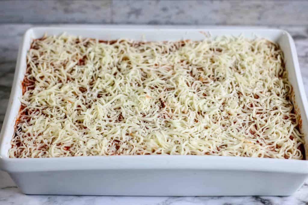 Cheese layered on top of sauce in white ceramic baking dish.