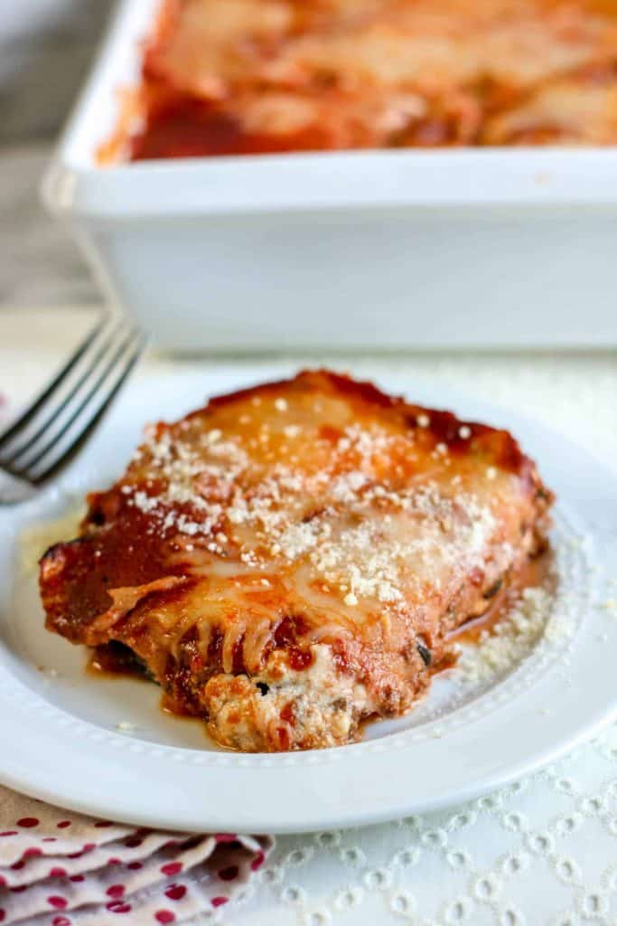 slice of eggplant lasagna on a white plate with large pan of lasagna in the background.
