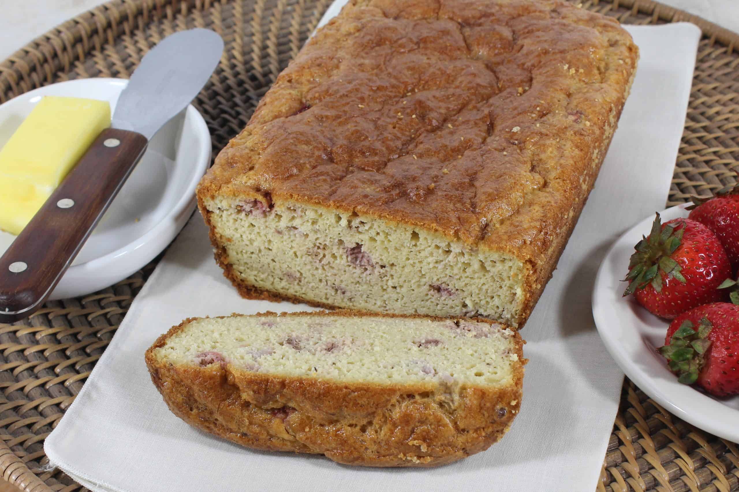 Keto Strawberry Bread on a cutting board with a stick of butter and knife on one side and a bowl of strawberries on the other side.