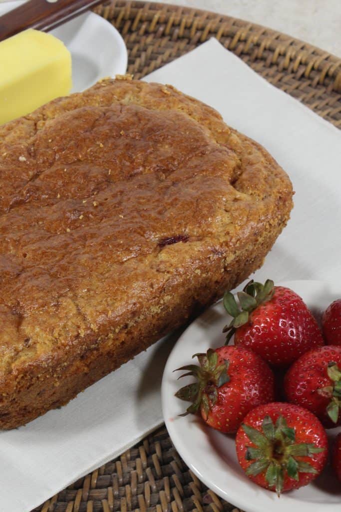 Angled shot of Strawberry Keto Bread with stick of butter on one side and bowl of strawberries on the other side.