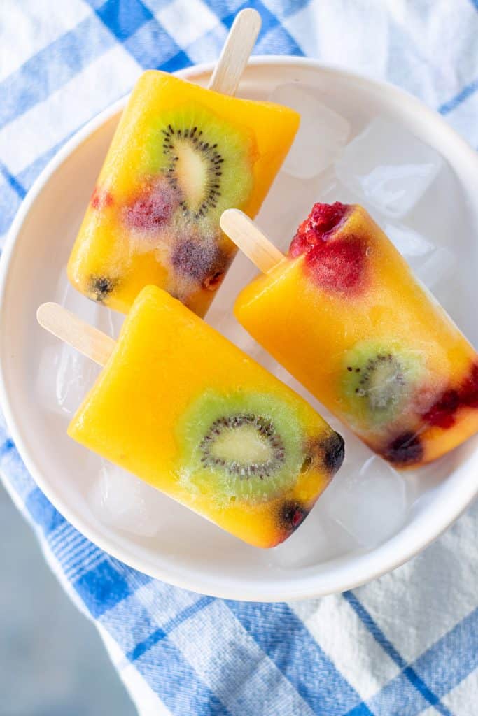 Overhead view of kiwi mango berry popsicles in a bowl of ice.