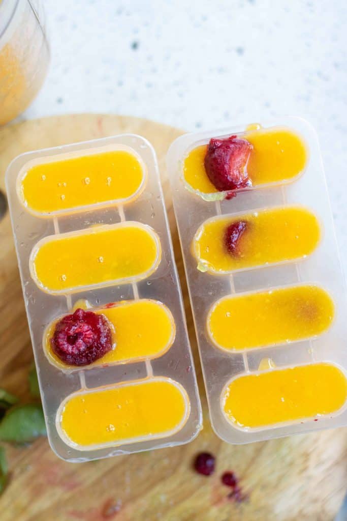 Mango popsicles in mold with berries on top.