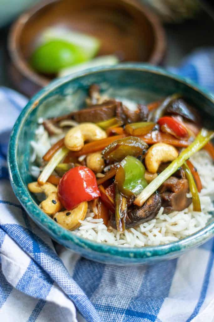 Angela shot of Kung Pao Vegetables over white rice in a blue bowl on a blue checked kitchen towel.