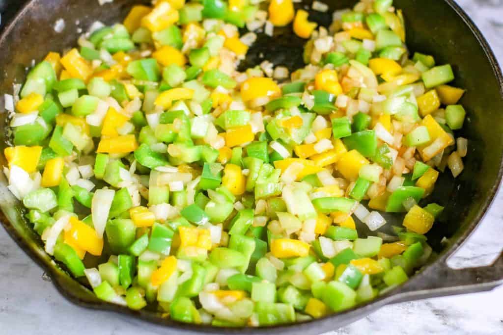 Sautéed bell peppers, onions and celery in a black iron skillet.