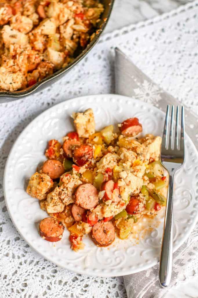 Overhead photo of Keto Jambalaya on a white plate with a black iron skillet with the jambalaya in the upper left hand corner.