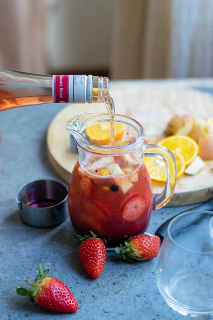 Wine being poured into pitcher with fruit and juice to make sangria.