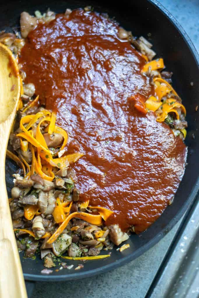 Ovehead closeup on tomato sauce on top of vegetables in a black iron skillet.
