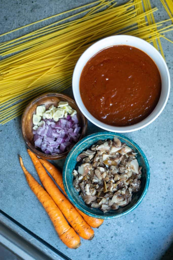 Overhead shot of tomato sauce, dry spaghetti, carrots, mushrooms, onions and garlic.
