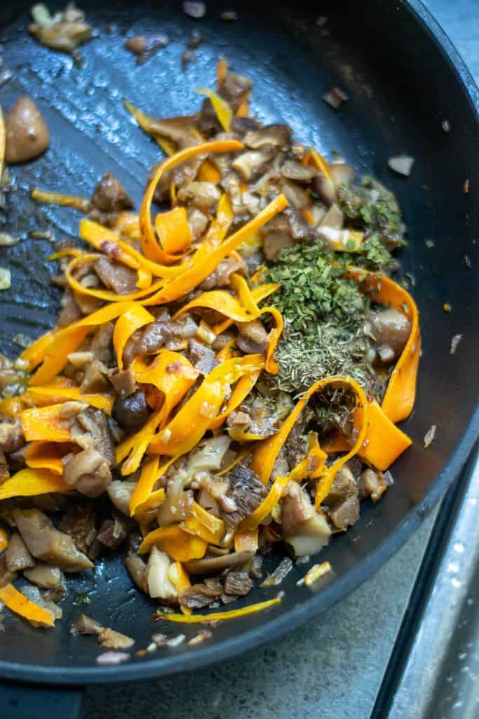 Carrots and mushrooms and herbs in a sauté pan.