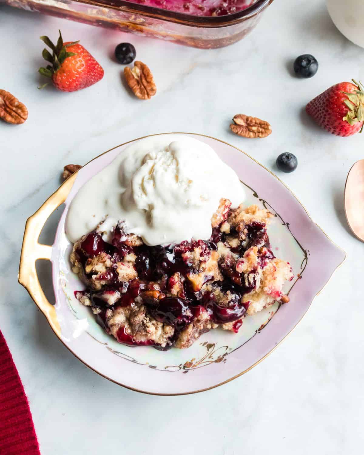 Blueberry strawberry dump cake served in a dish with vanilla ice cream on top